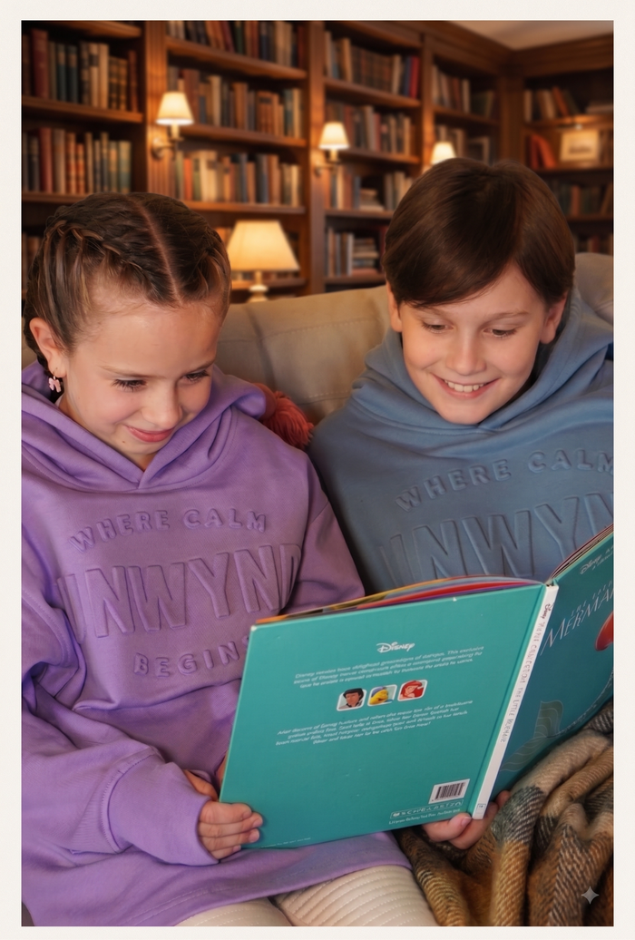 girl wearing a hoodie reading a book while sitting on a sofa